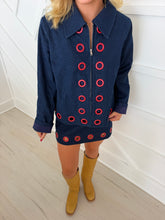 Load image into Gallery viewer, Pretty Follies dark blue denim shorts with red eyelets, styled with a matching jacket and light brown boots.